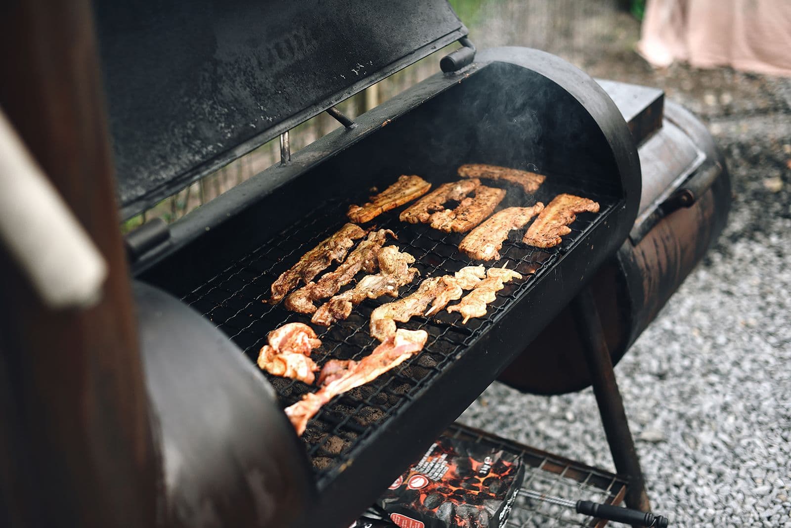 Close-up of meat cooking on an outdoor barbecue grill with rising smoke