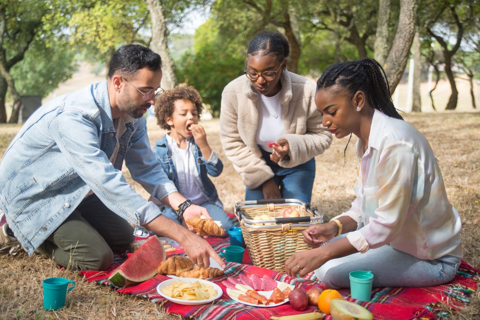 A large family gathering at outdoor picnic tables under a park pavilion