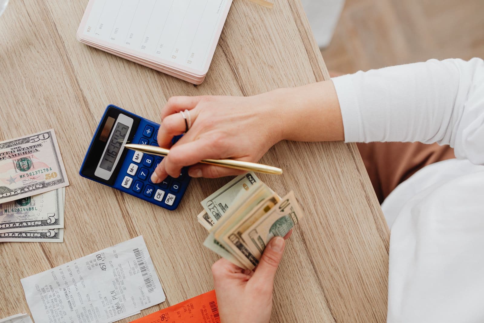 A person calculating expenses with a calculator, notebook, and receipts on a table