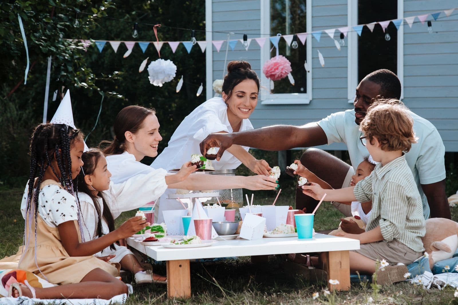 A lively backyard gathering with family and friends sharing food outdoors at picnic tables